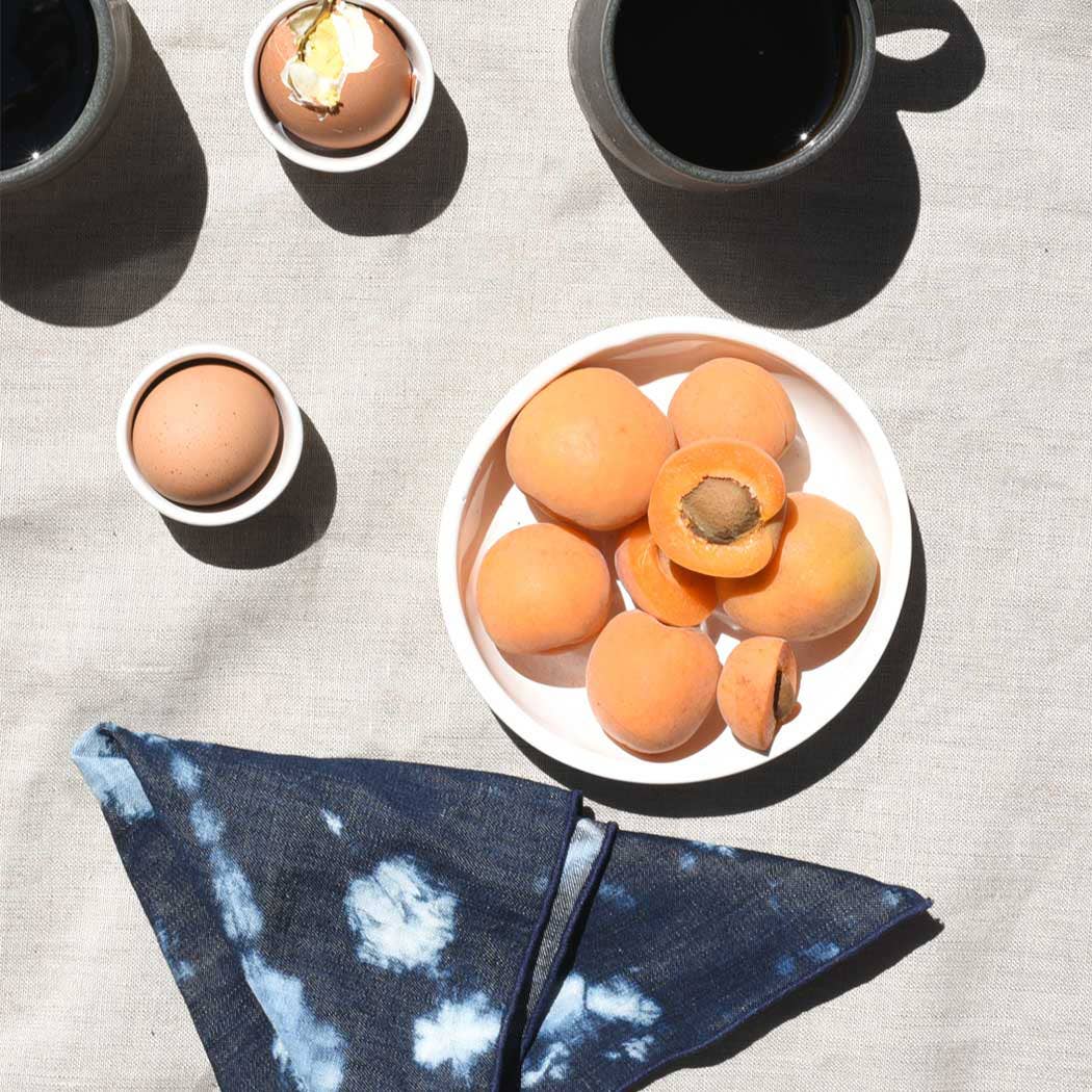 Bowl of apricots with eggs and a tie-dye Atelier Saucier napkin on a textured surface | socius design