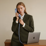 Person in a suit holding a blue POP Phone receiver with a laptop in the background